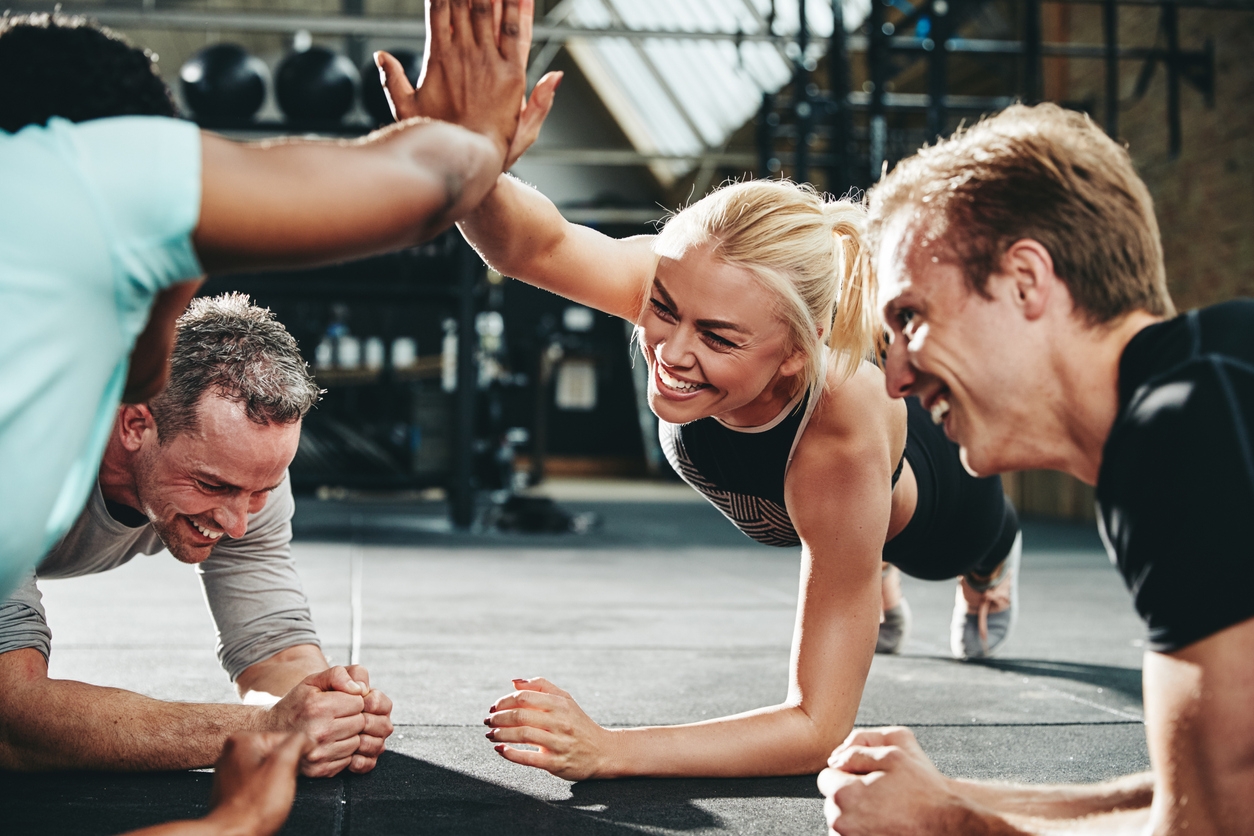 Fitness Insurance - Two laughing young women in sportswear high fiving together during a planking class at the gym with a couple of male friends