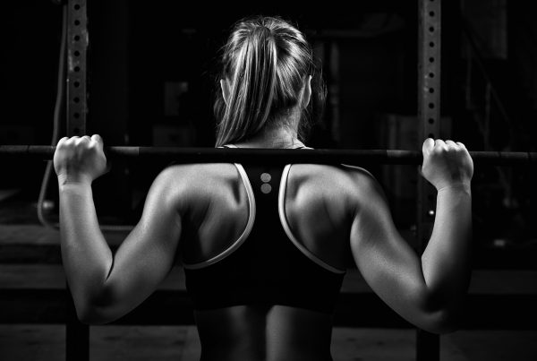 Squat - image of the back view young female doing barbell squats in gym