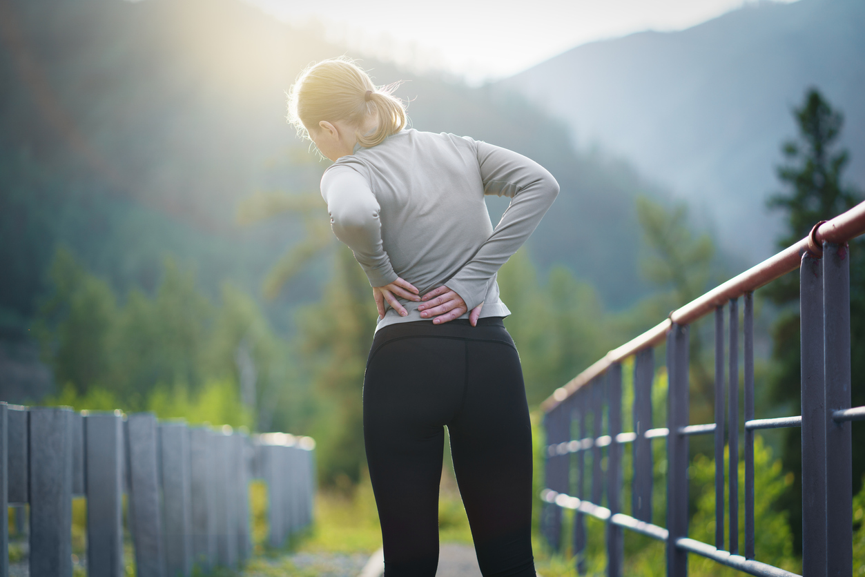 Pain-free mindset - Image of woman on a bridge massaging her painful back due to sports injury