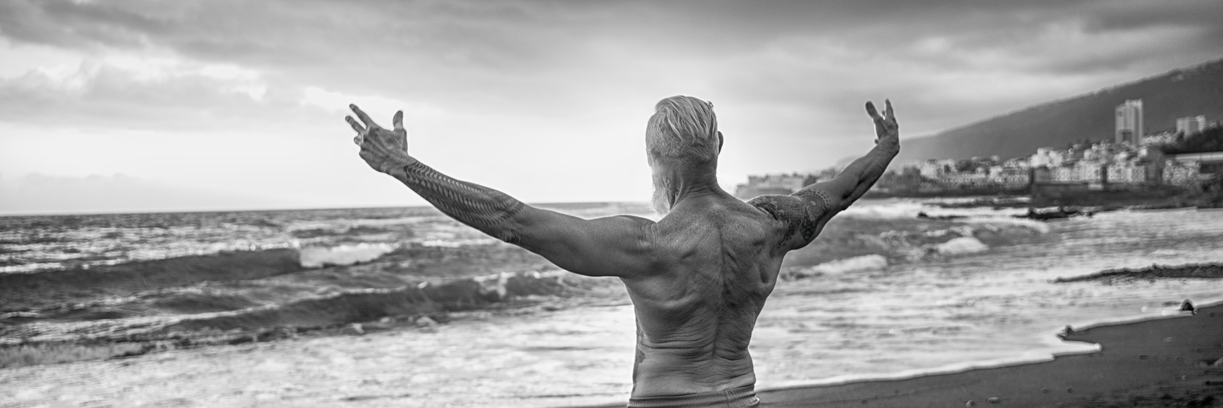 Back training - Image of senior man showing his muscular fit body with tattoos on the beach.