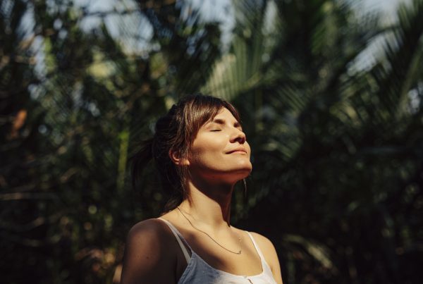 Relaxation - Close up image of happy young woman looking relaxed. She is pictured with her eyes closed with a serene look on her face amongst palm trees