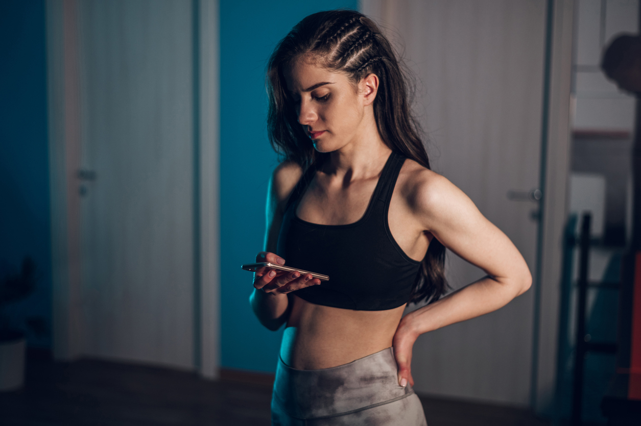 Class cover - Image of young woman using a smartphone while dressed in fitness clothes at home. She looks thoughtful and a little concerned.