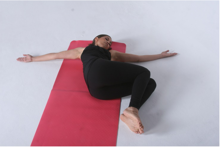Image of Torso Rotation Assessment - this shows a woman laying on her back with her arms stretched out to her sides. She has her leg bent and lowered to one side on the floor.