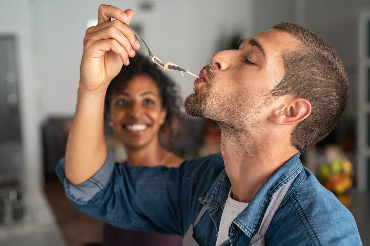 Mood and food - Image of man tasting spaghetti pasta while smiling woman looks at him.