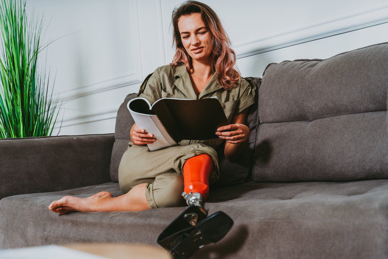 Image of woman with leg prosthesis reading on a grey sofa reading
