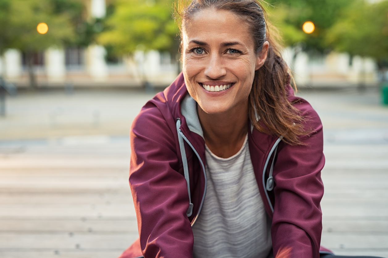 Putting yourself first - Image of smiling woman sitting on floor of city street after exercising.