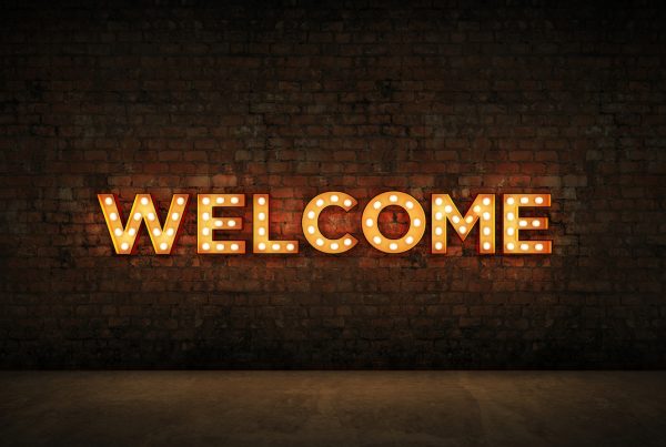 Welcome the 'almost active' - Image of a brick wall with a huge neon sign saying 'WELCOME' on it.