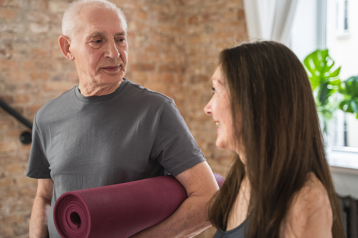 Stroke survivors - Image of two older people on their way to a class. The gentleman looks a little more serious, he has a rolled up mat under his left arm. The lady looks cheerful - she could be the instructor of the class.