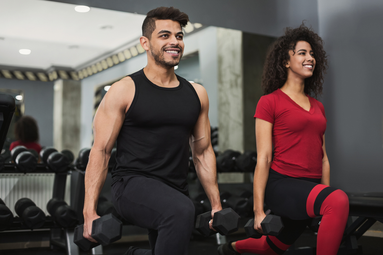Two people smiling performing lunges with dumbbells