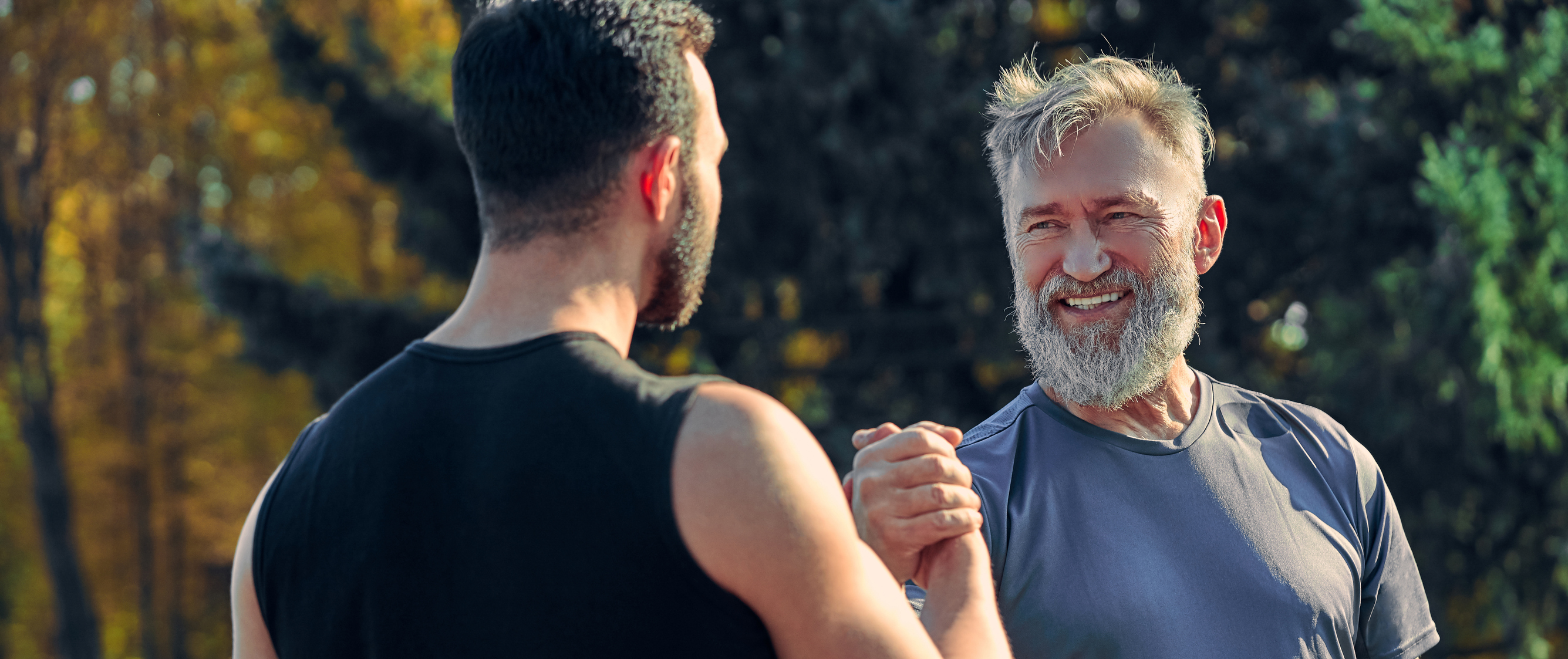 Long-term conditions - Image of two happy different aged sportsmen greeting each other outdoors