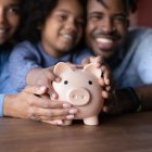 financial concepts - Image of family smiling and holding on to a piggy bank