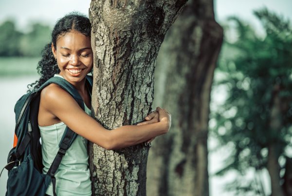 Mental Health - Image of a woman looking serene and happy whilst hugging a tree