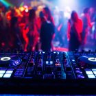 making music for fitness classes - Image of controller DJ mixer in a nightclub at a party against the background of blurred silhouettes of dancing people