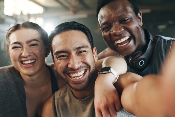 Three people smiling directly at the camera - thay are in fitness gear. It looks like they are at the end of their workout.