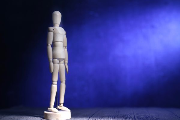 Assessing and correcting posture. Wooden doll standing still under the light, against a blue background.