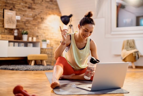 Training in small spaces - smiling woman getting ready to workout at home whilst watching her laptop