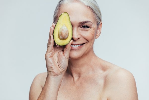 Longevity through nutrition - image of smiling woman holding up an avocado in front of one of her eyes